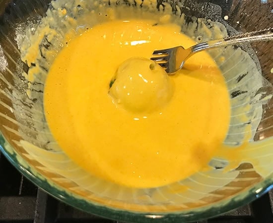 potato ball being dipped  in besan batter using a fork