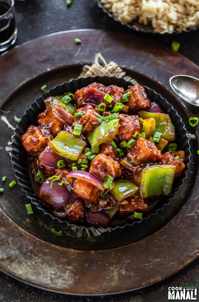 restaurant style chilli paneer served in black plate and brown rice served in the background