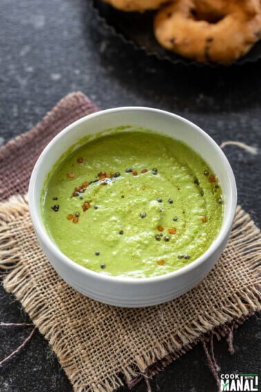 bowl of green color coconut chutney with few vadas placed in the background