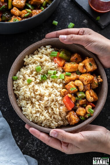 pair of hands holding a bowl of honey cashew tofu