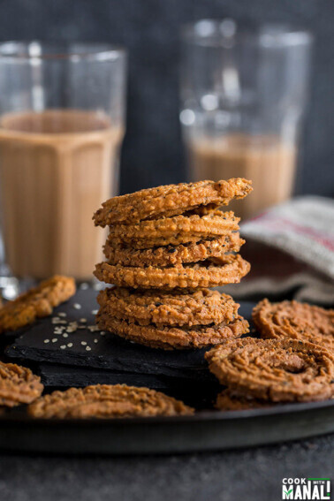 stack of chakli on a black plate and glasses of chai in the background