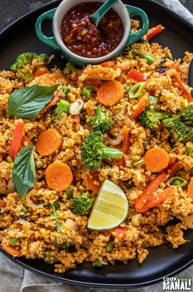 quinoa with veggies and basil and a lime wedge with a small bowl of hot sauce placed on the side