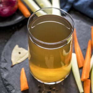 vegetable stock in a glass container with veggies on the side